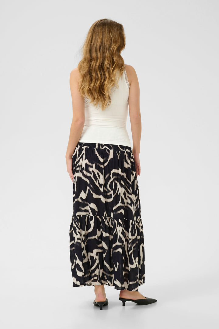 Femme vue de dos portant une camisole blanche et une jupe longue à motifs abstraits.