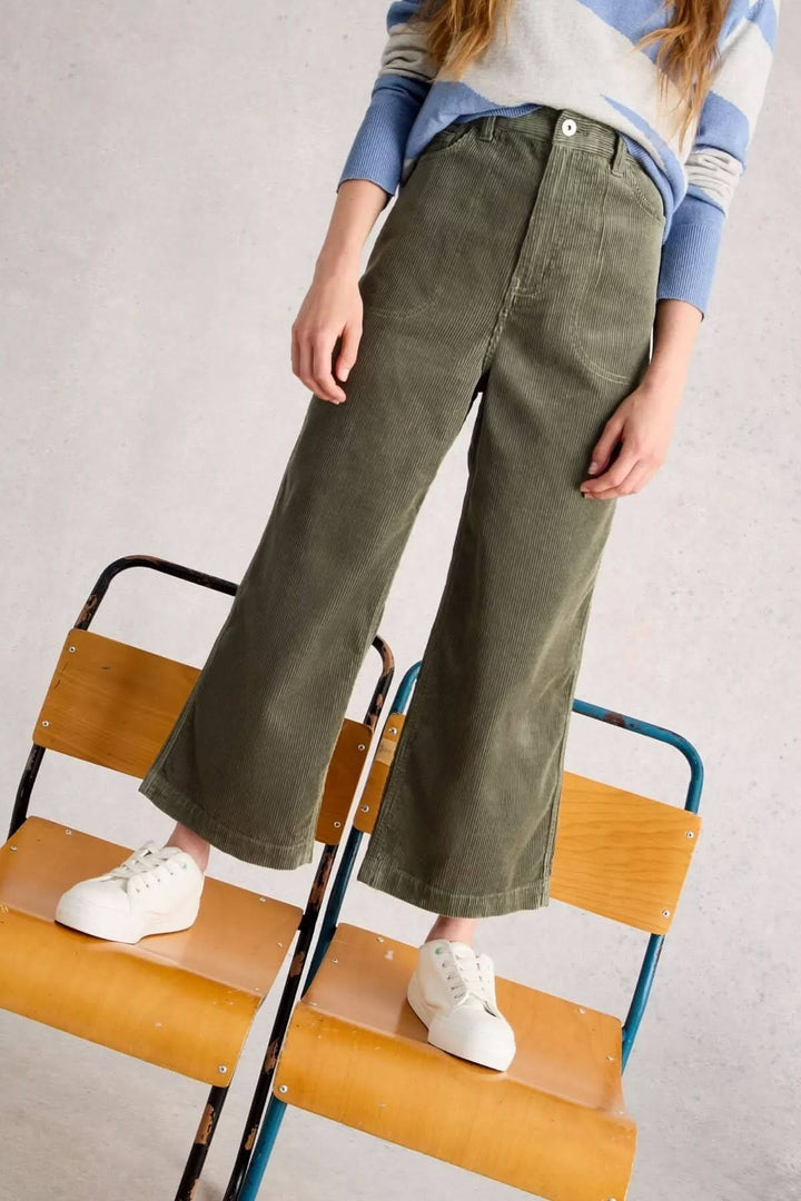 Pantalon Tia en velours côtelé vert, coupe évasée et taille haute, porté avec des baskets blanches pour un look moderne et décontracté.