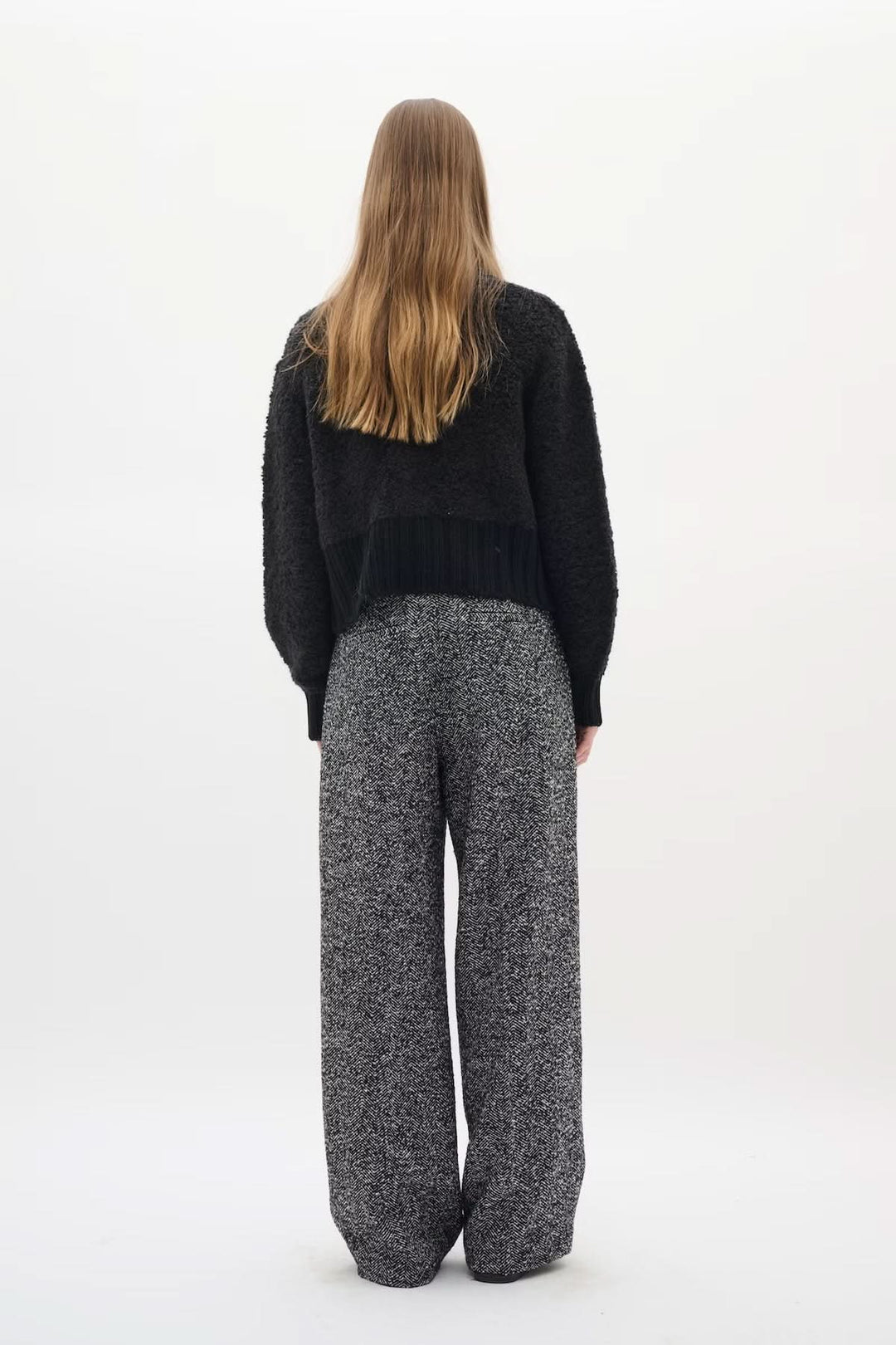 Dos d'une femme portant le Cardigan Guo noir, coupe courte structurée, avec pantalon large gris. Élégance moderne et sophistiquée.