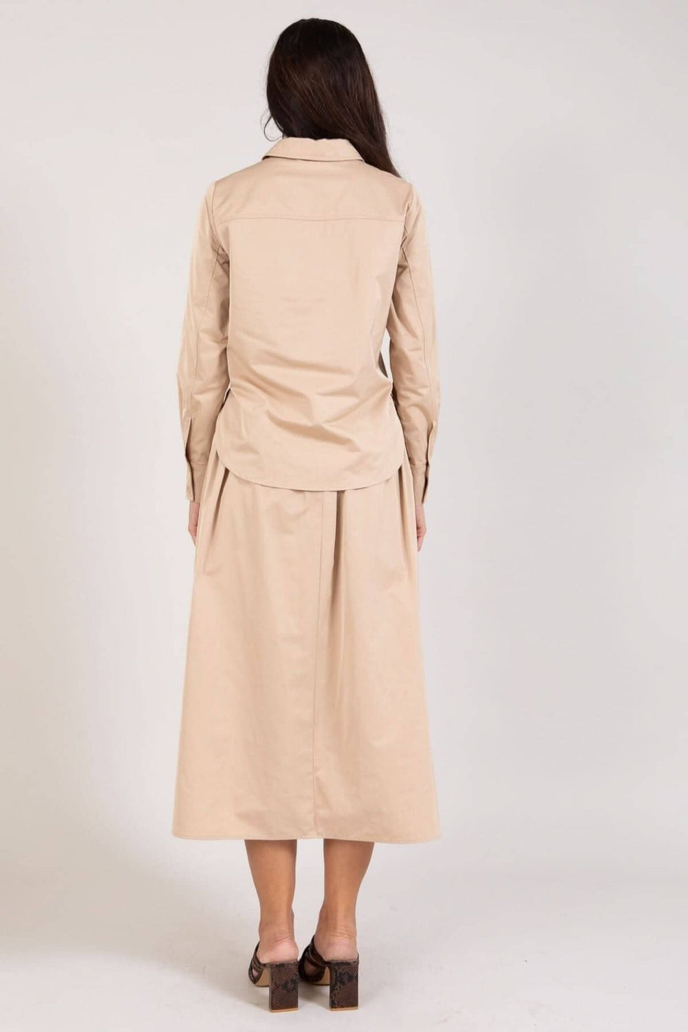 Femme vue de dos portant une jupe longue beige et une chemise assortie, style élégant et décontracté.