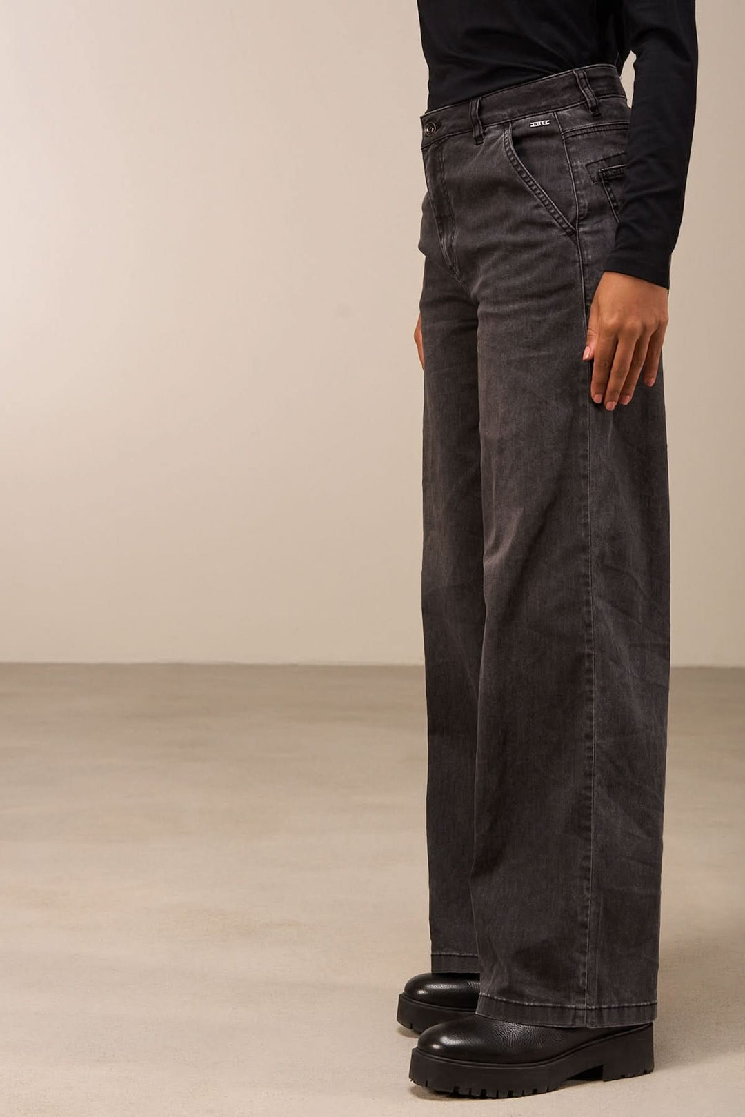 Jean coupe large gris avec taille mi-haute et jambes amples, porté avec une blouse noire.