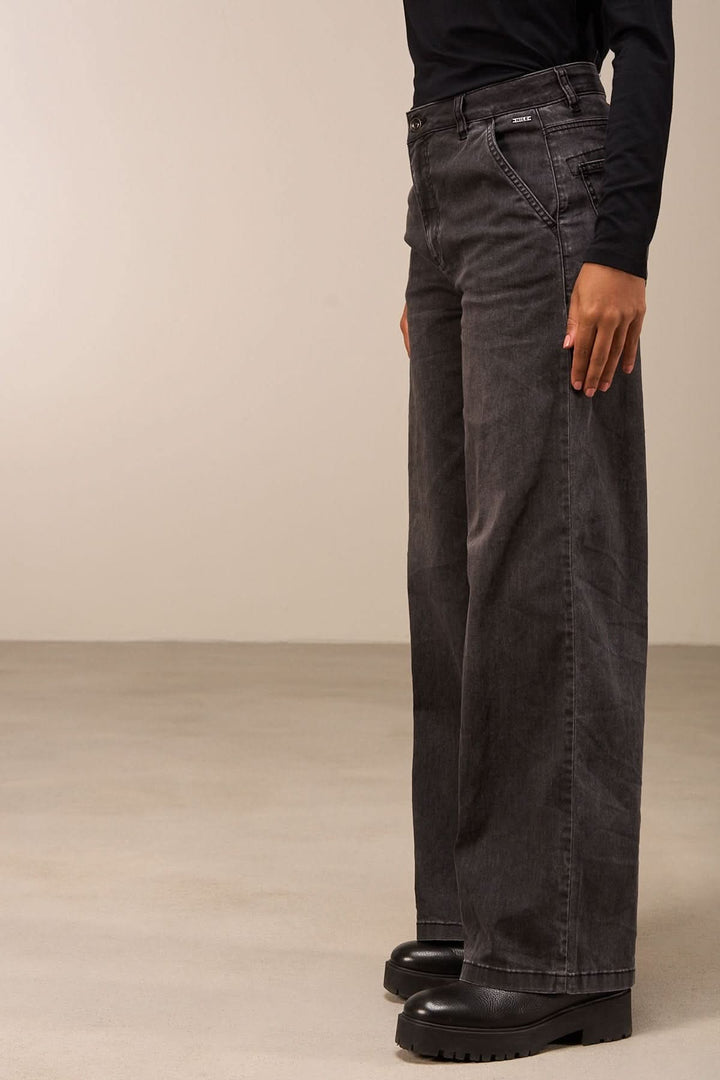 Jean coupe large gris avec taille mi-haute et jambes amples, porté avec une blouse noire.