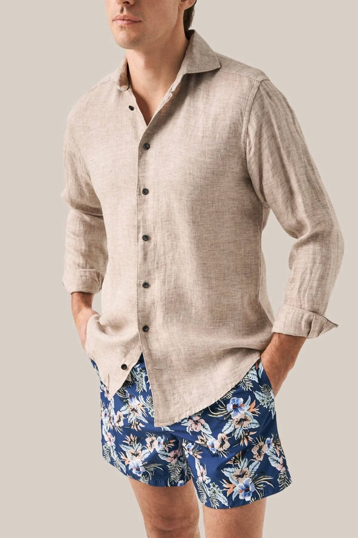 Homme portant une chemise en lin et un maillot de bain fleuri à motifs dans un style décontracté.