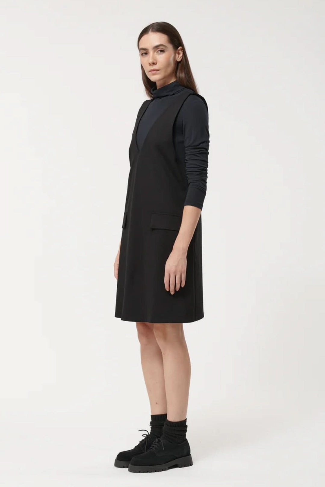 Robe sans manches chic à encolure en V et coupe évasée, portée avec un sous-pull noir pour un look minimaliste et polyvalent.