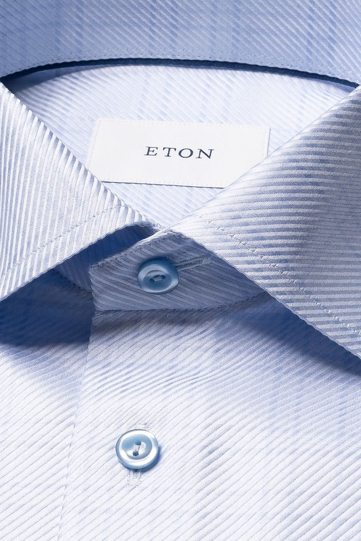 Chemise en coton bleu clair à carreaux fins avec col ouvert et boutons, offrant une élégance moderne et un confort texturé.