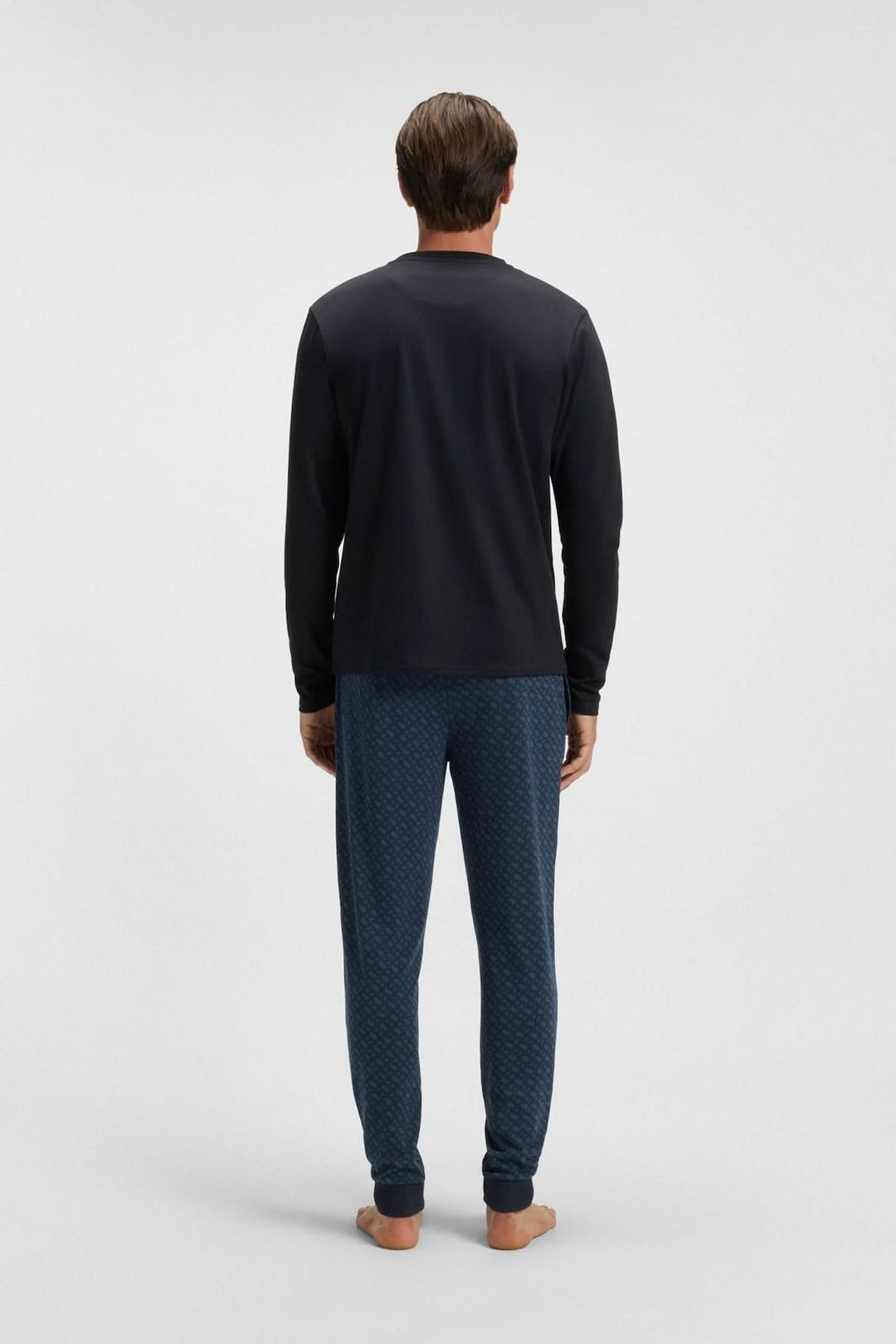 Homme portant un ensemble pyjama en coton avec logo BOSS, vu de dos, composé d'un haut noir et d'un pantalon bleu à motifs.