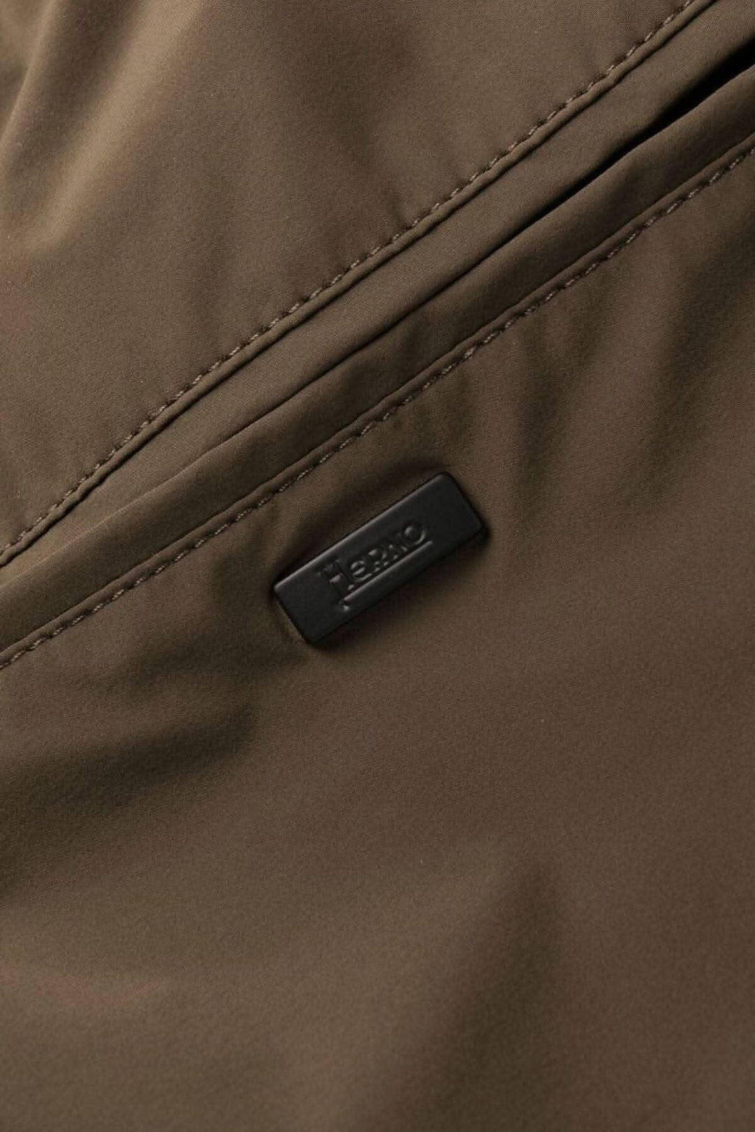 Détail d'une étiquette en cuir sur un pantalon en nylon, couleur marron, de la collection Herno Laminar.