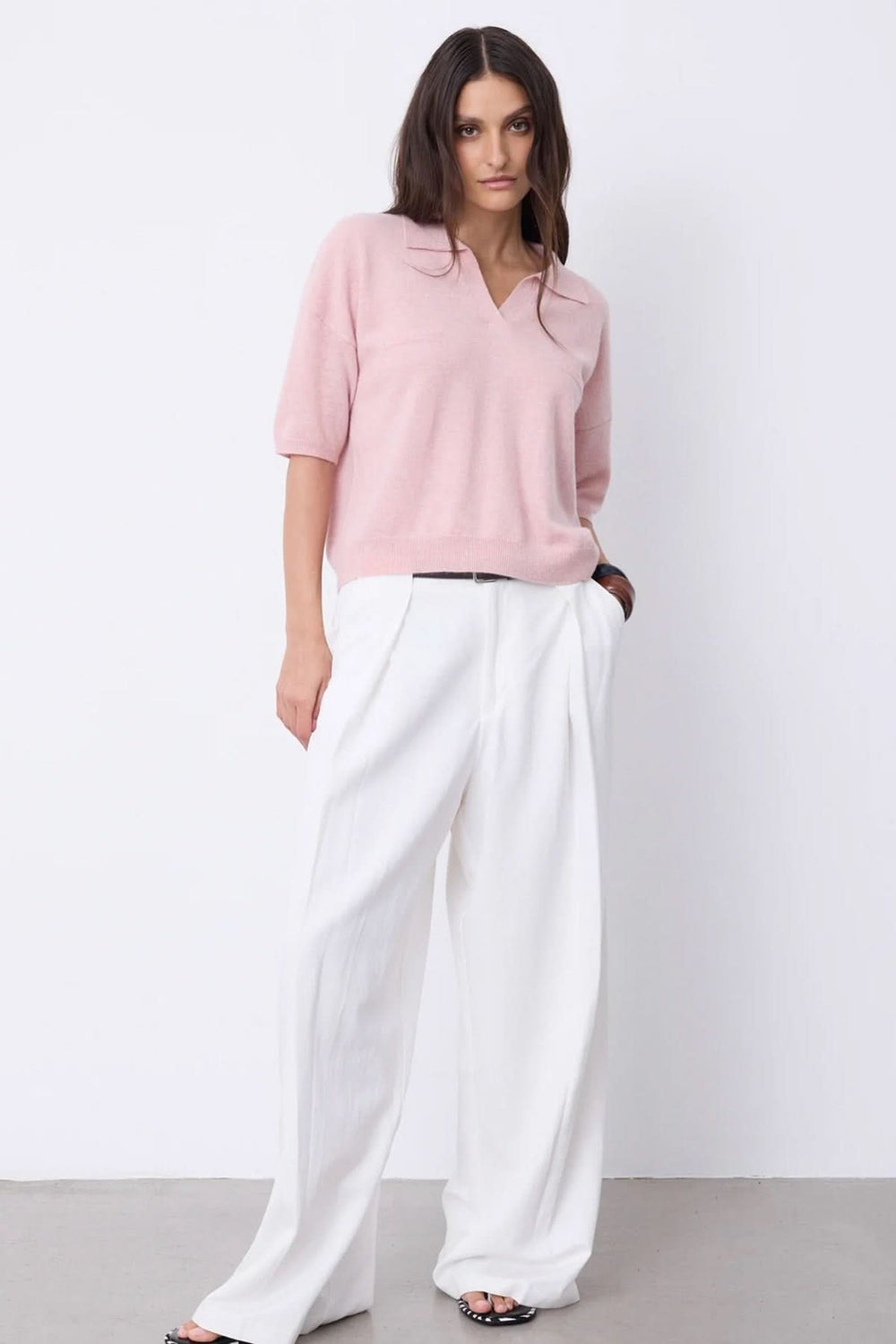 Femme en polo à manches courtes rose avec encolure en V et pantalon blanc, look estival chic.