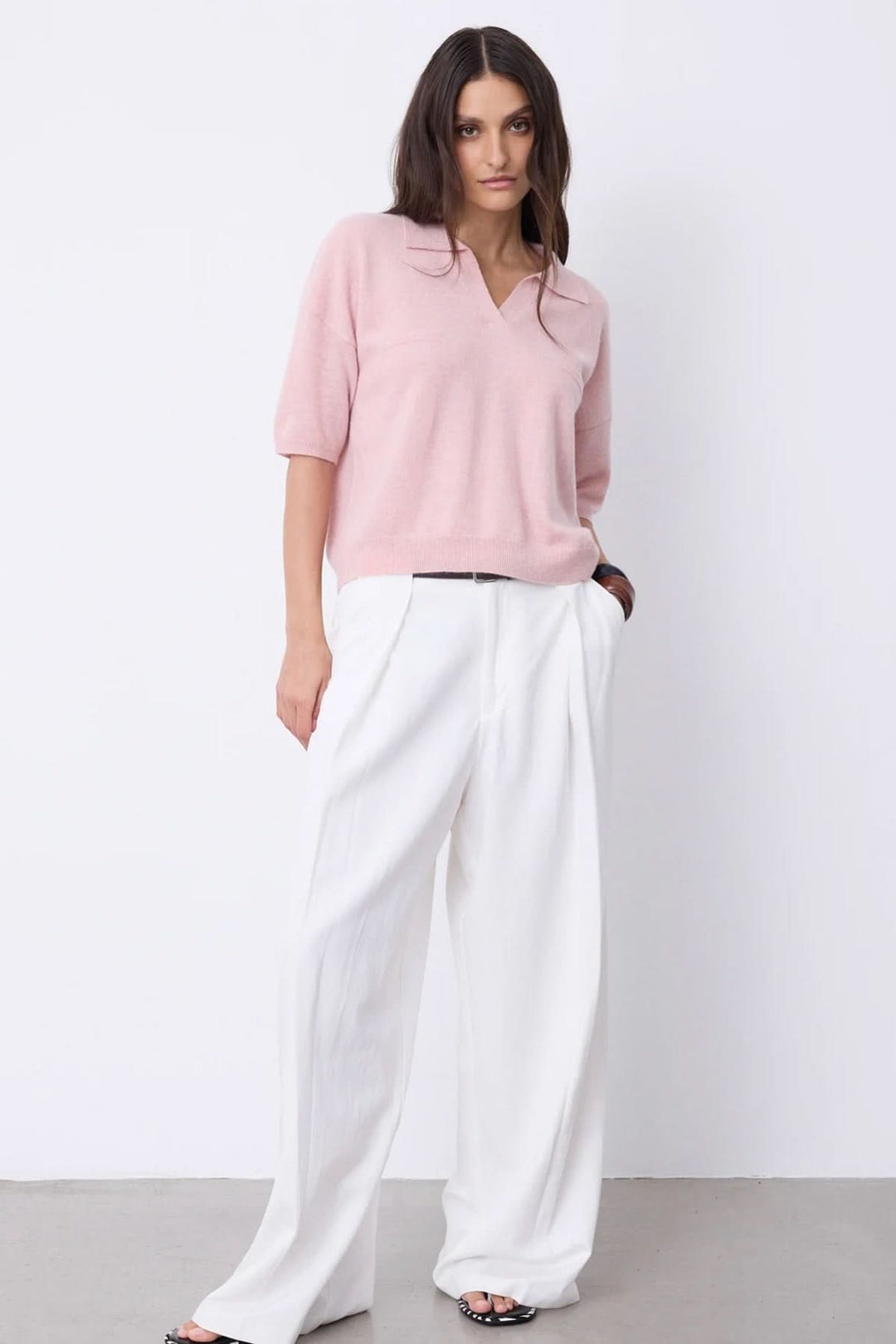 Femme en polo à manches courtes rose avec encolure en V et pantalon blanc, look estival chic.