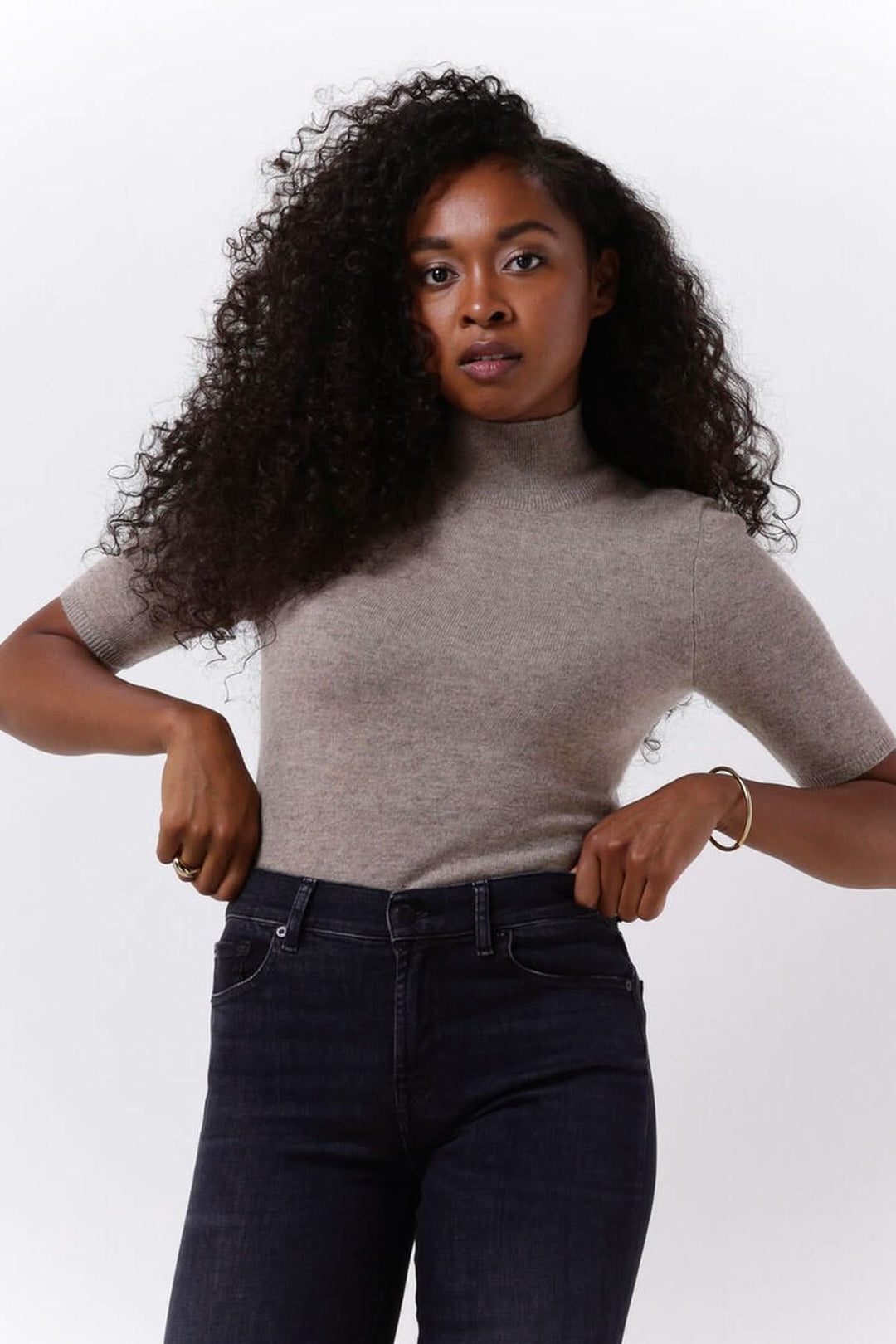 Femme portant un chandail col montant manches courtes — maille fine élégante, stylisé avec un jean foncé.