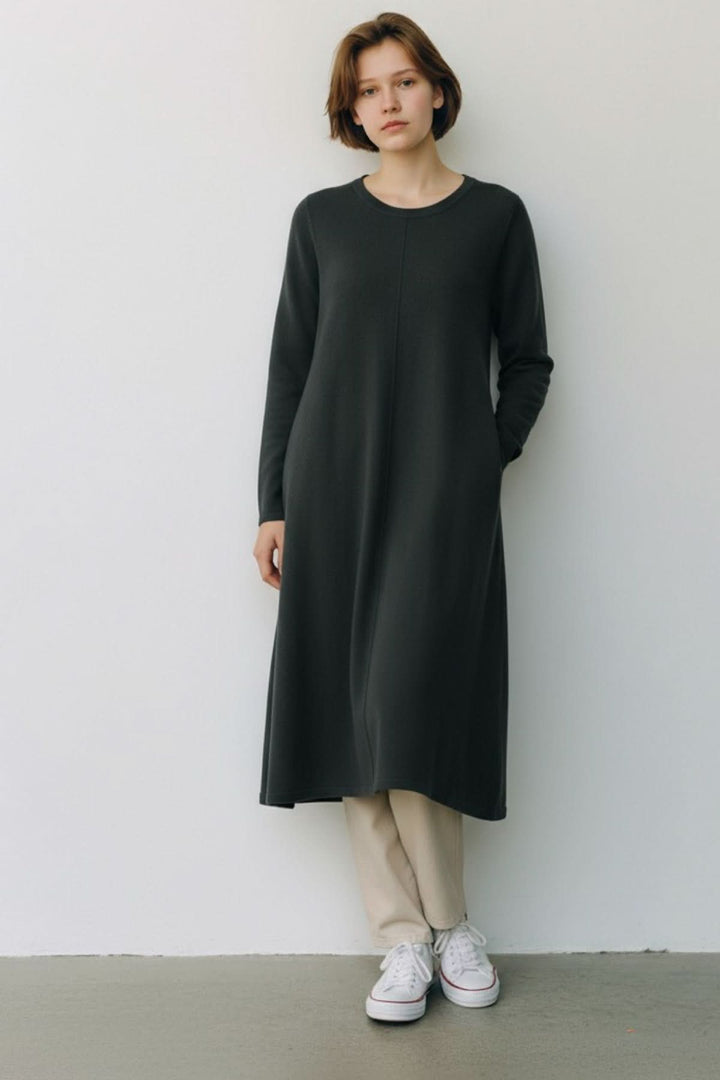 Femme portant une robe de tricot à manches longues, coupe fluide, encolure ronde, ligne verticale au centre, élégante et confortable.