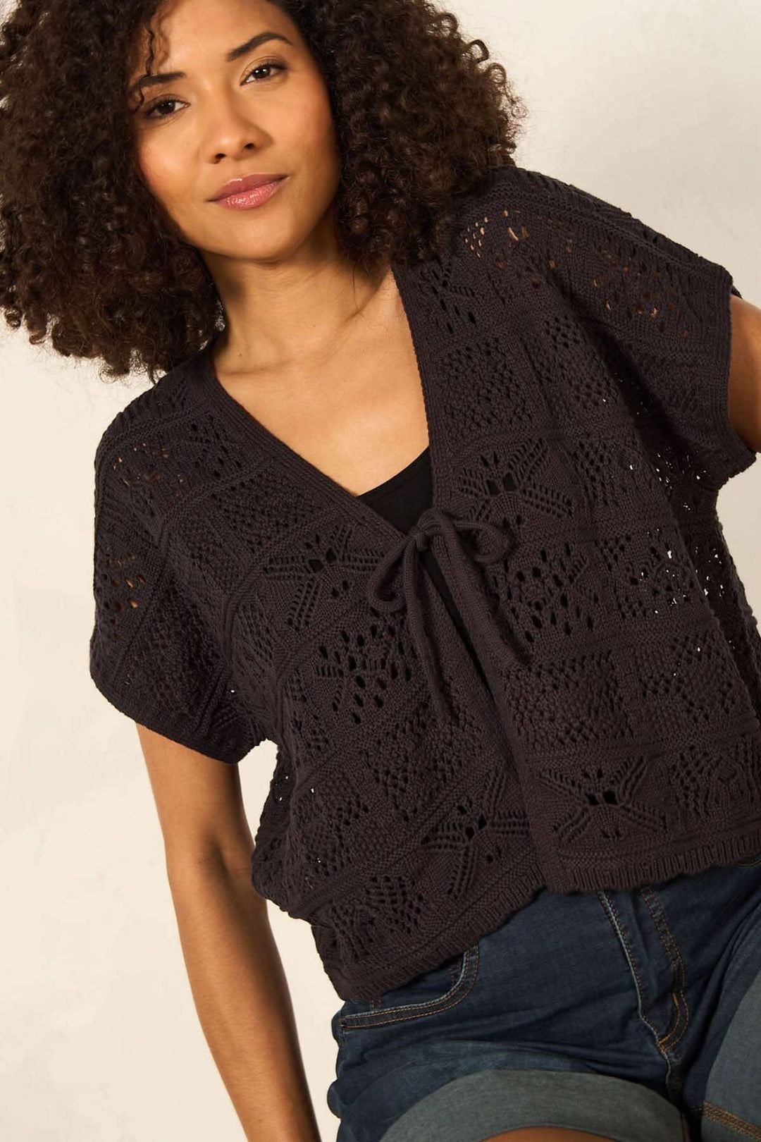 Cardigan en maille ajourée à manches courtes, fermé par un ruban, présenté par un modèle avec des boucles.