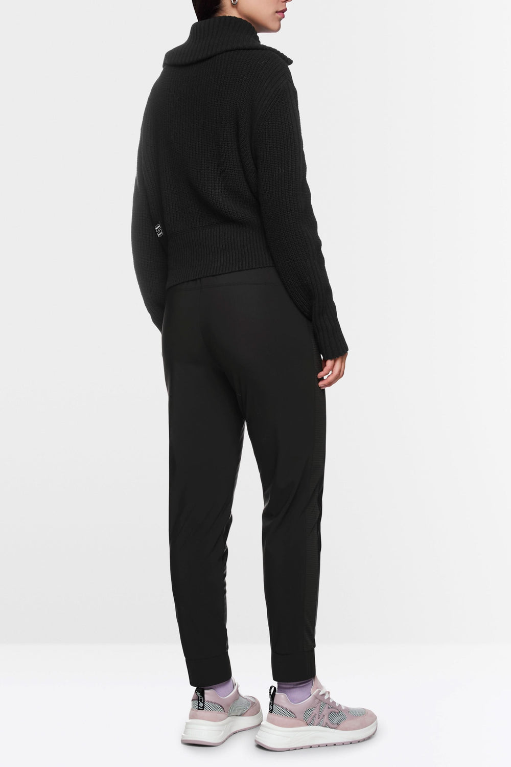 Femme de dos portant un pantalon habillé Rhodos avec un pull noir et des baskets, look moderne et décontracté.