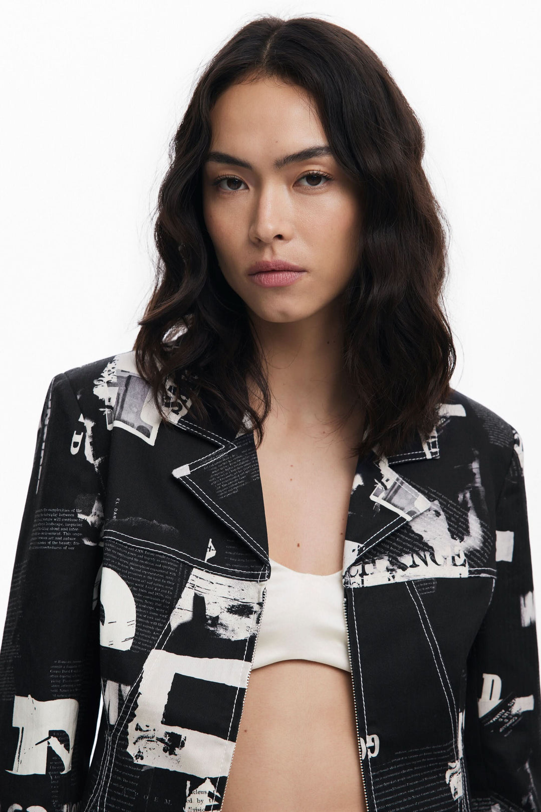 Veste style motard à imprimé typographique, coupe structurée, look audacieux, portée avec un top et cheveux ondulés.