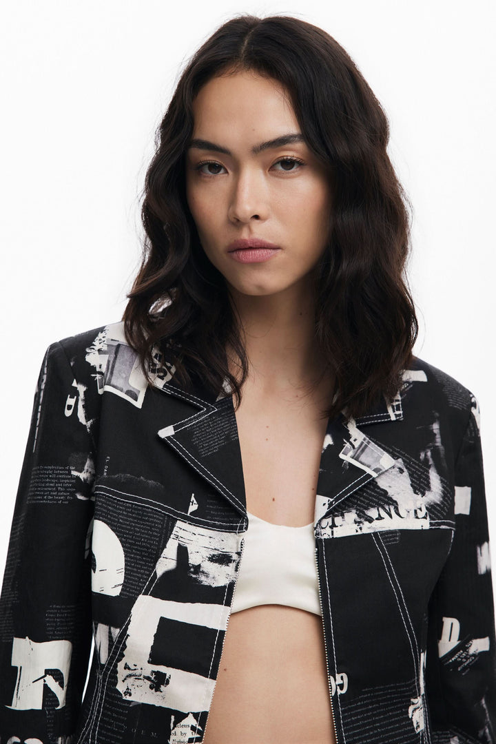 Veste style motard à imprimé typographique, coupe structurée, look audacieux, portée avec un top et cheveux ondulés.
