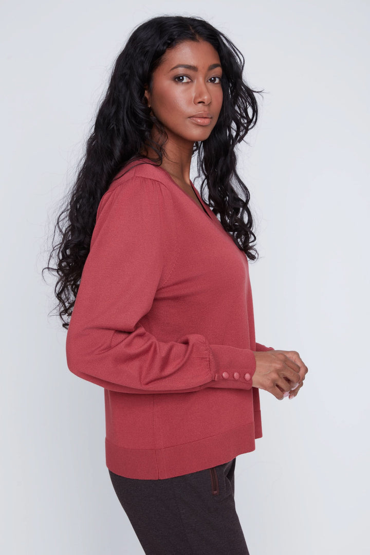 Chandail encolure en V, manches bouffantes, élégant et féminin, porté avec un pantalon, sur fond neutre.