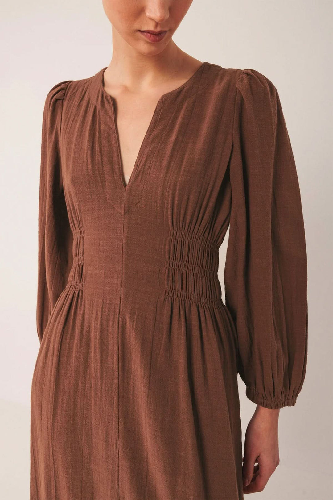 Femme portant une robe longue à encolure V et manches bouffantes avec smocks à la taille, ajoutant une touche élégante et féminine.