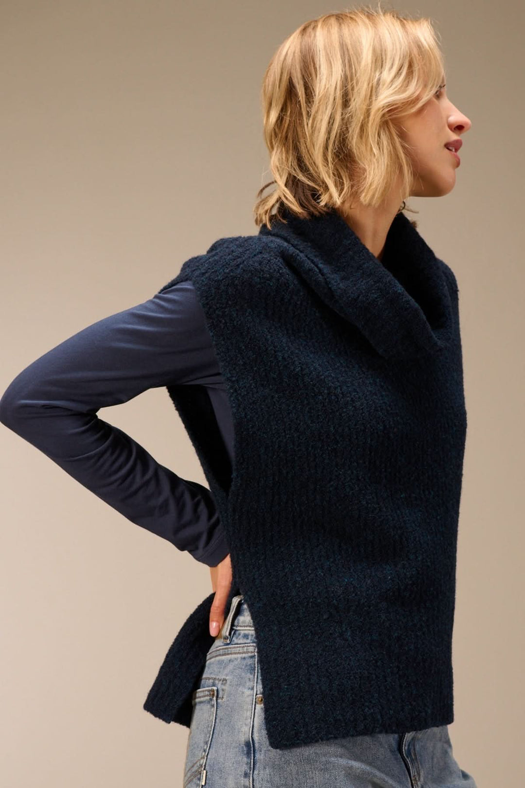 Gilet sans manches en maille bouclée à col drapé porté sur t-shirt à manches longues, vue de côté.