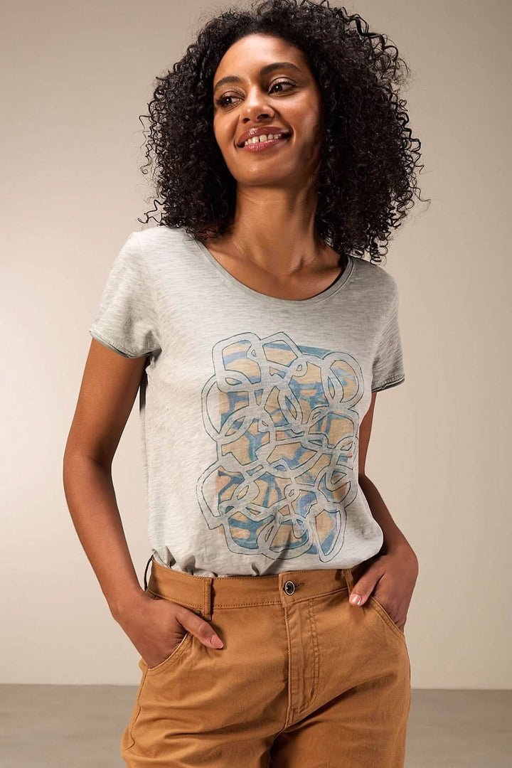 T-shirt à manches courtes avec un imprimé artistique graphique sur le devant, porté par une femme souriante.