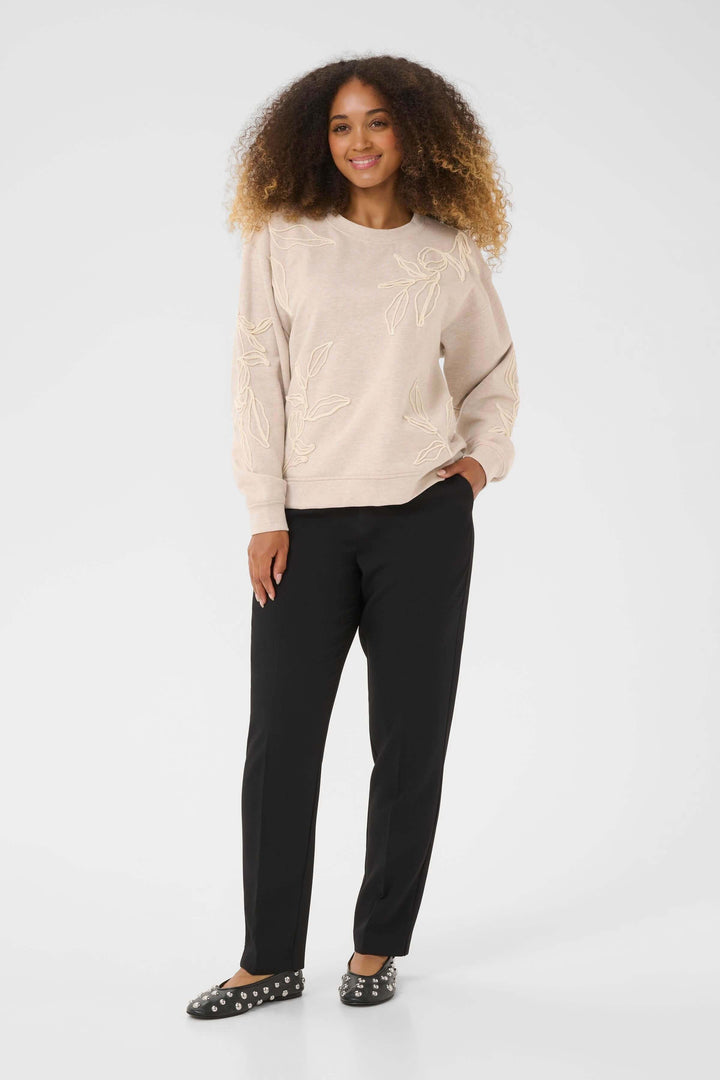 Femme portant le Chandail Lovisa en coton ouaté à broderies ton sur ton pour un look décontracté et élégant, avec motif floral délicat.