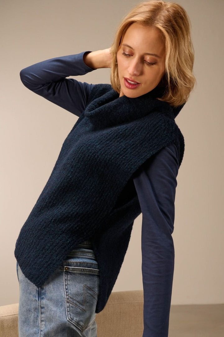 Gilet sans manches en maille bouclée à col drapé porté par modèle sur t-shirt à manches longues, montrant coupe boîte et col enveloppant.