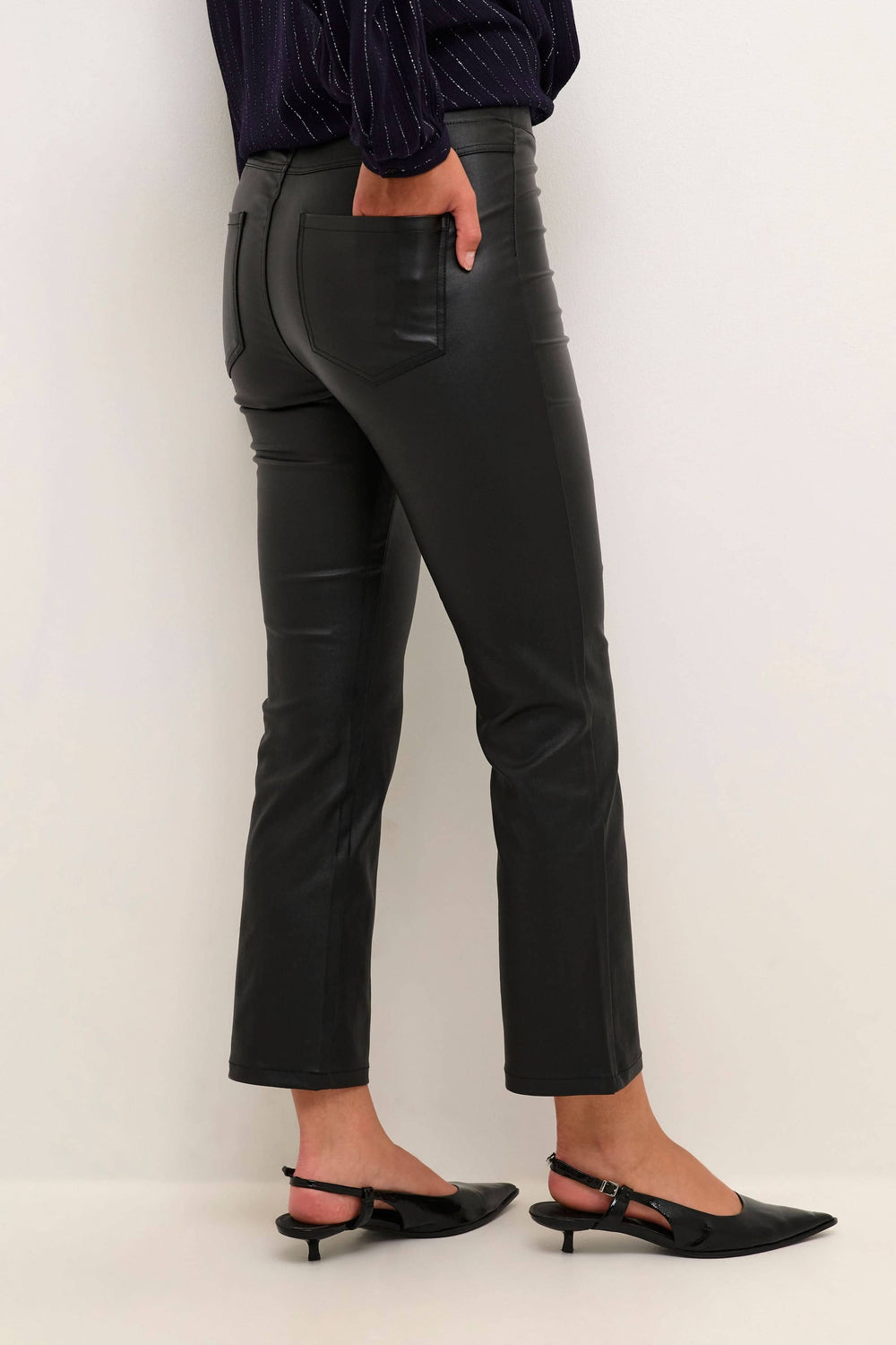 Pantalon noir en simili cuir, coupe ajustée au-dessus de la cheville, porté avec des chaussures à talons.