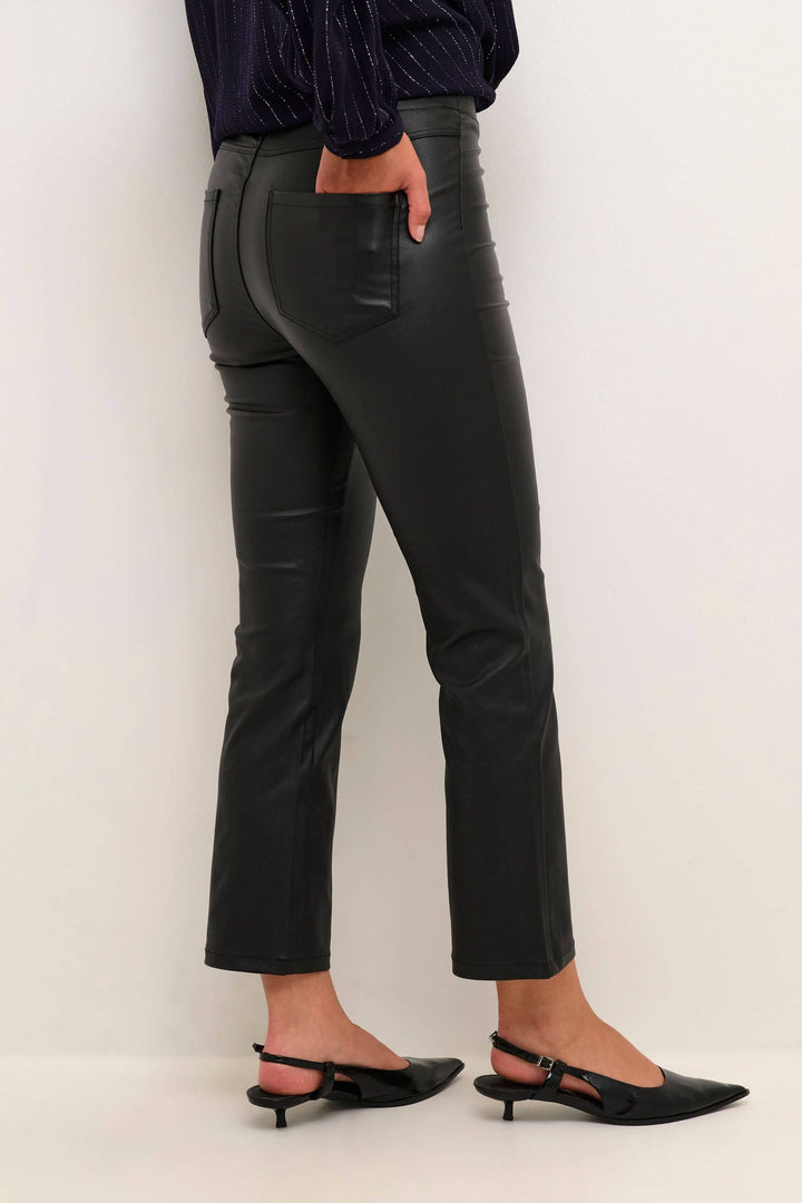 Pantalon noir en simili cuir, coupe ajustée au-dessus de la cheville, porté avec des chaussures à talons.