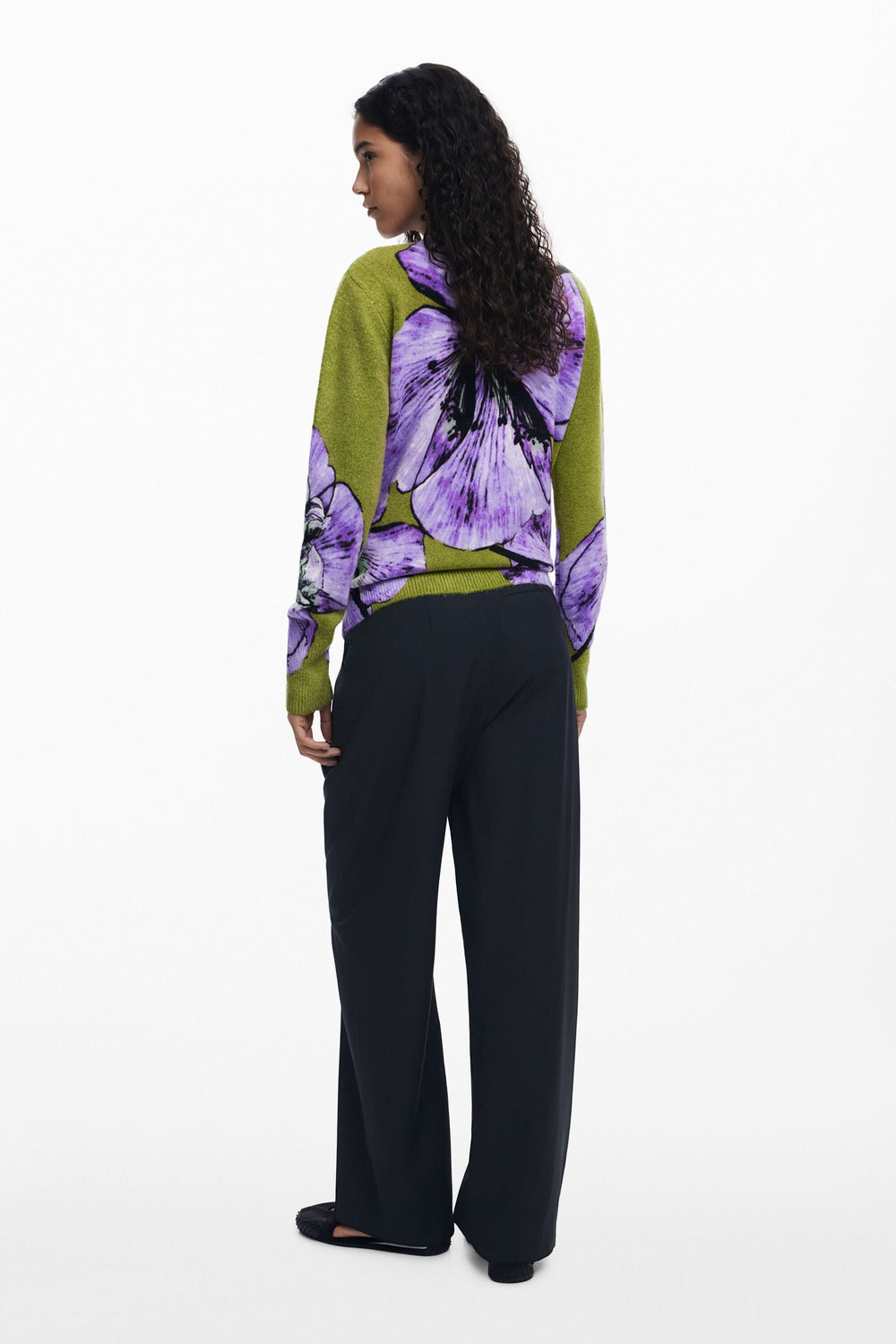 Femme de dos portant un chandail floral oversize vibrant avec un pantalon noir, créant un look artistique.