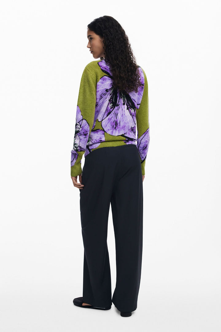 Femme de dos portant un chandail floral oversize vibrant avec un pantalon noir, créant un look artistique.