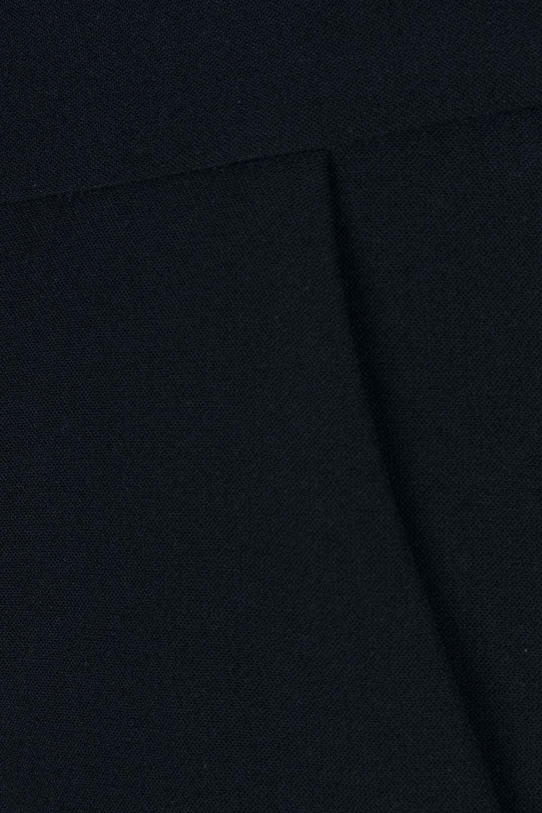 Détail d'un pantalon habillé à jambe large en tissu noir, mettant en valeur sa taille haute et plis marqués.