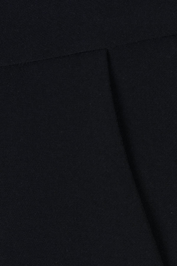 Détail d'un pantalon habillé à jambe large en tissu noir, mettant en valeur sa taille haute et plis marqués.