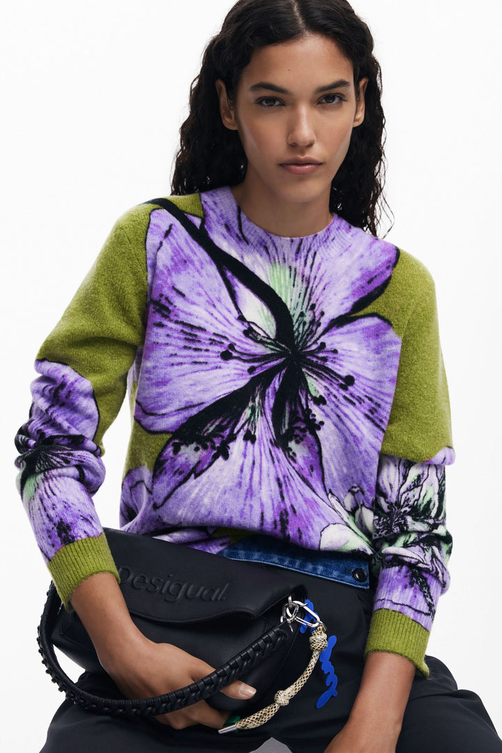 Chandail floral à col rond, imprimé oversize violet et vert, porté avec sac noir et style artistique.