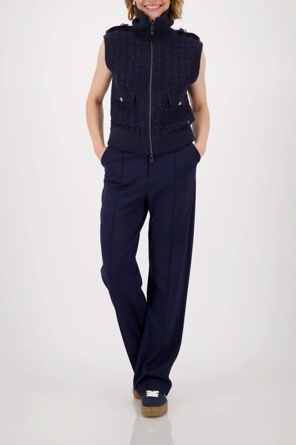 Veste sans manches zippée en maille texturée avec col montant et poches à rabat, portée sur un pantalon élégant.