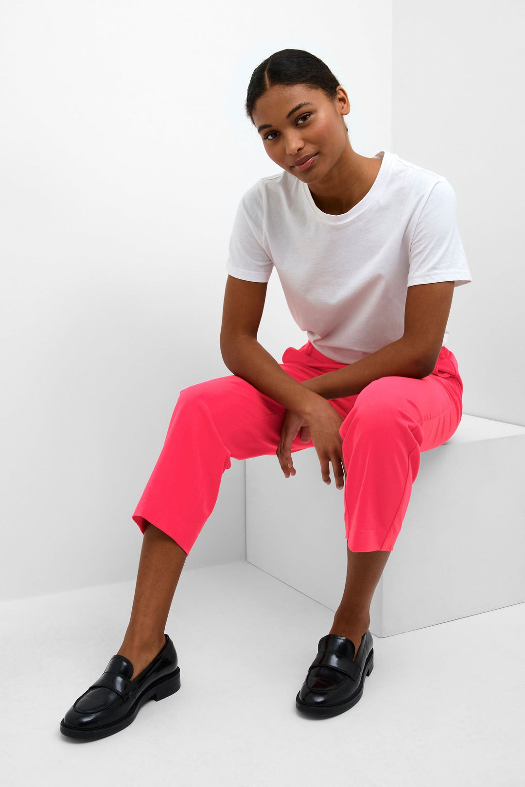 Femme portant un pantalon court sakura rose, t-shirt blanc, assise sur un banc, style professionnel chic.
