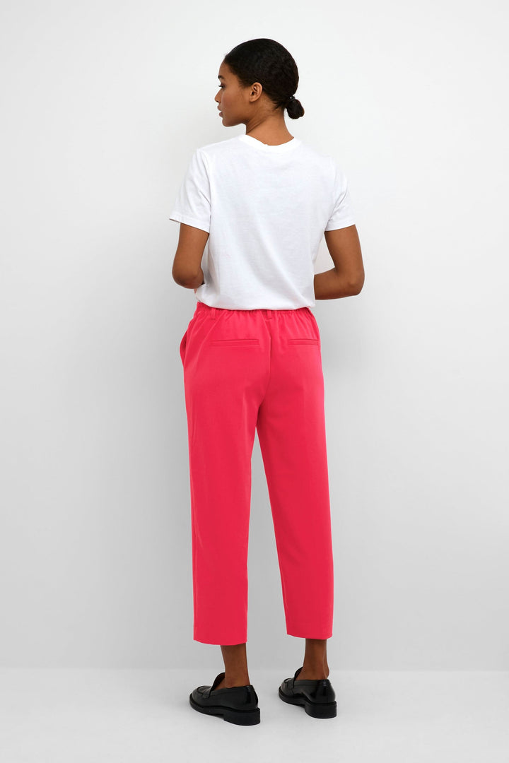 Femme vue de dos portant un pantalon court rose et un t-shirt blanc, avec des poches arrière.