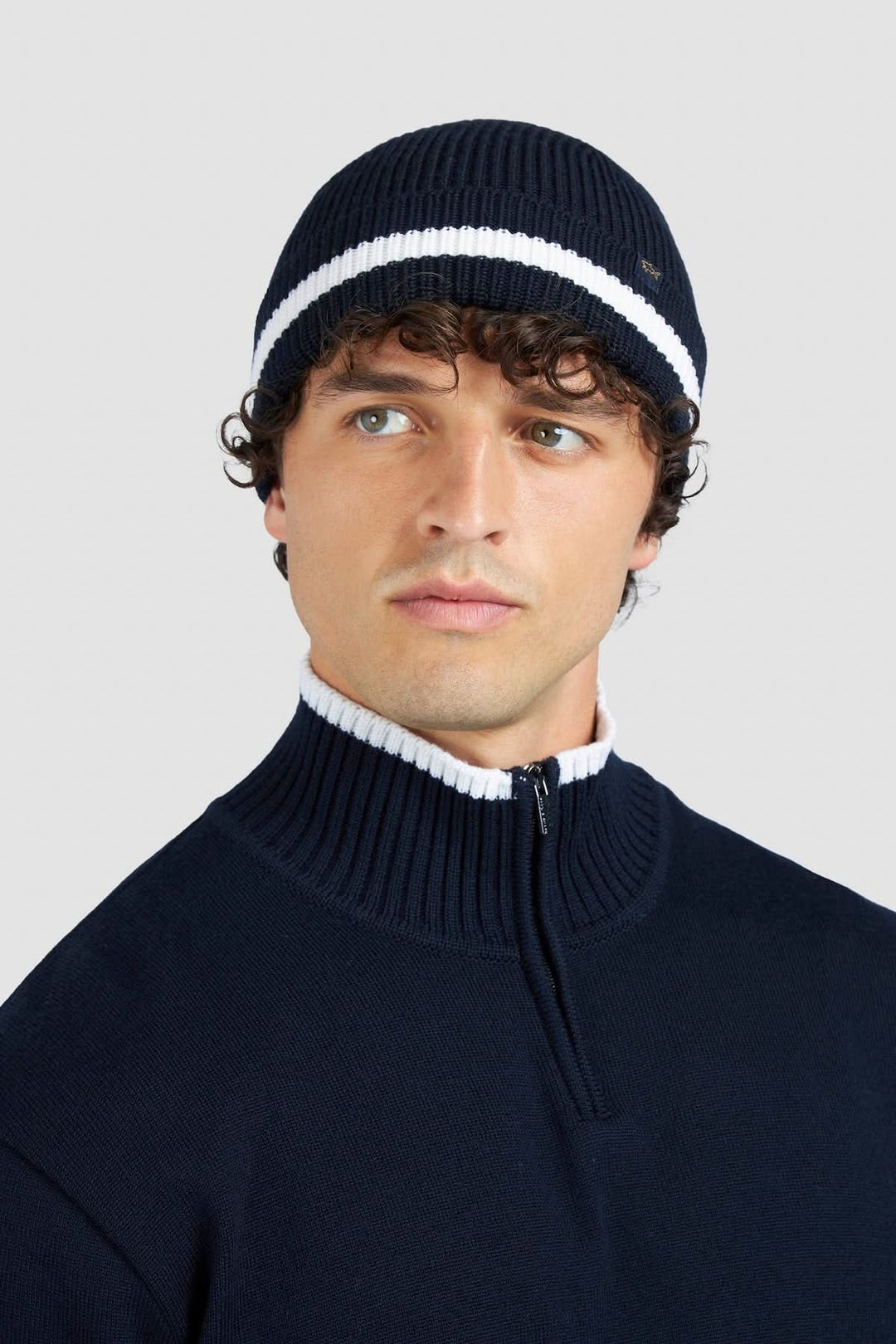 Homme portant un chandail à demi-fermeture et un bonnet en tricot bleu marine, style sportif chic.