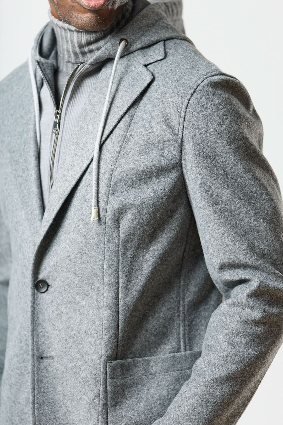 Veston hybride à capuche gris avec capuche à cordons, porté sur un col roulé en laine fouillée, style urbain élégant.