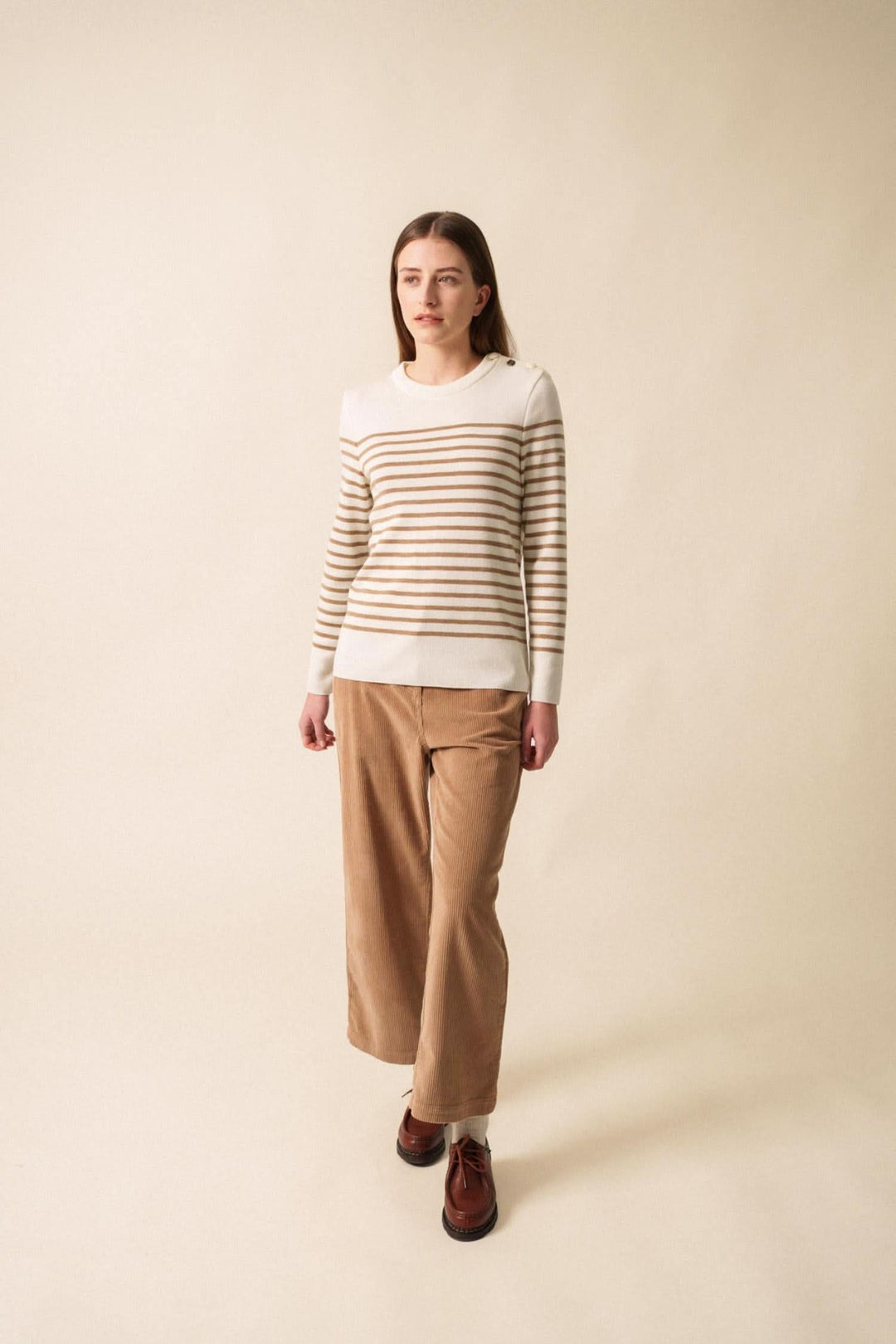 Modèle portant un chandail marinière à rayures beige et blanc avec un pantalon en velours, style automnal décontracté.