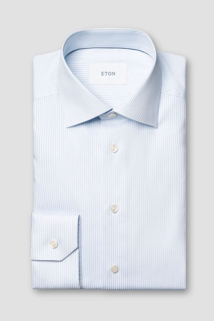 Chemise rayée en coton et lyocell avec fines rayures bleues et col italien structuré, allongée sur un fond gris clair.