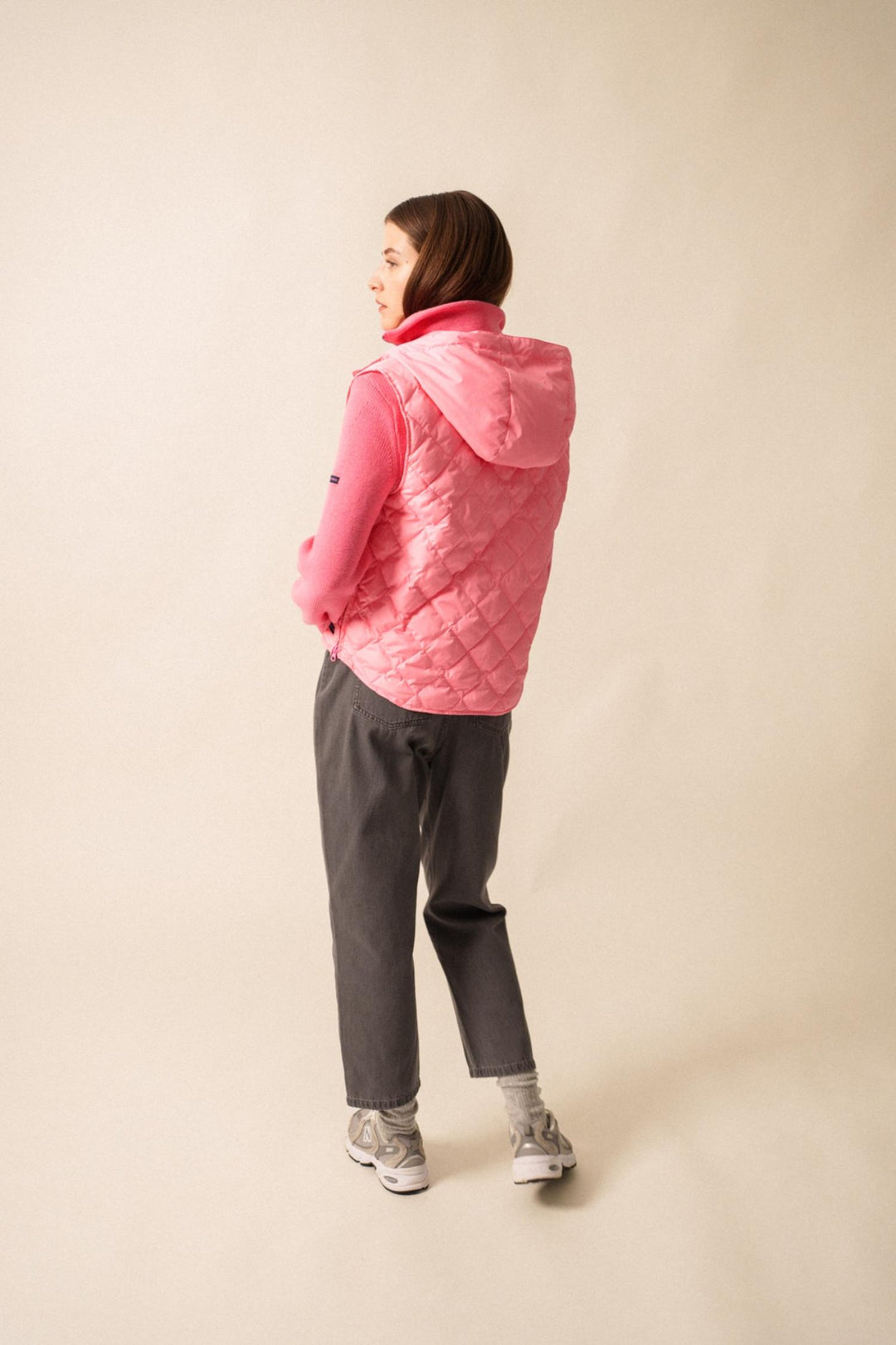 Vue arrière d'une femme en doudoune sans manche rose, associée à un pull, pour un look urbain et sportif.