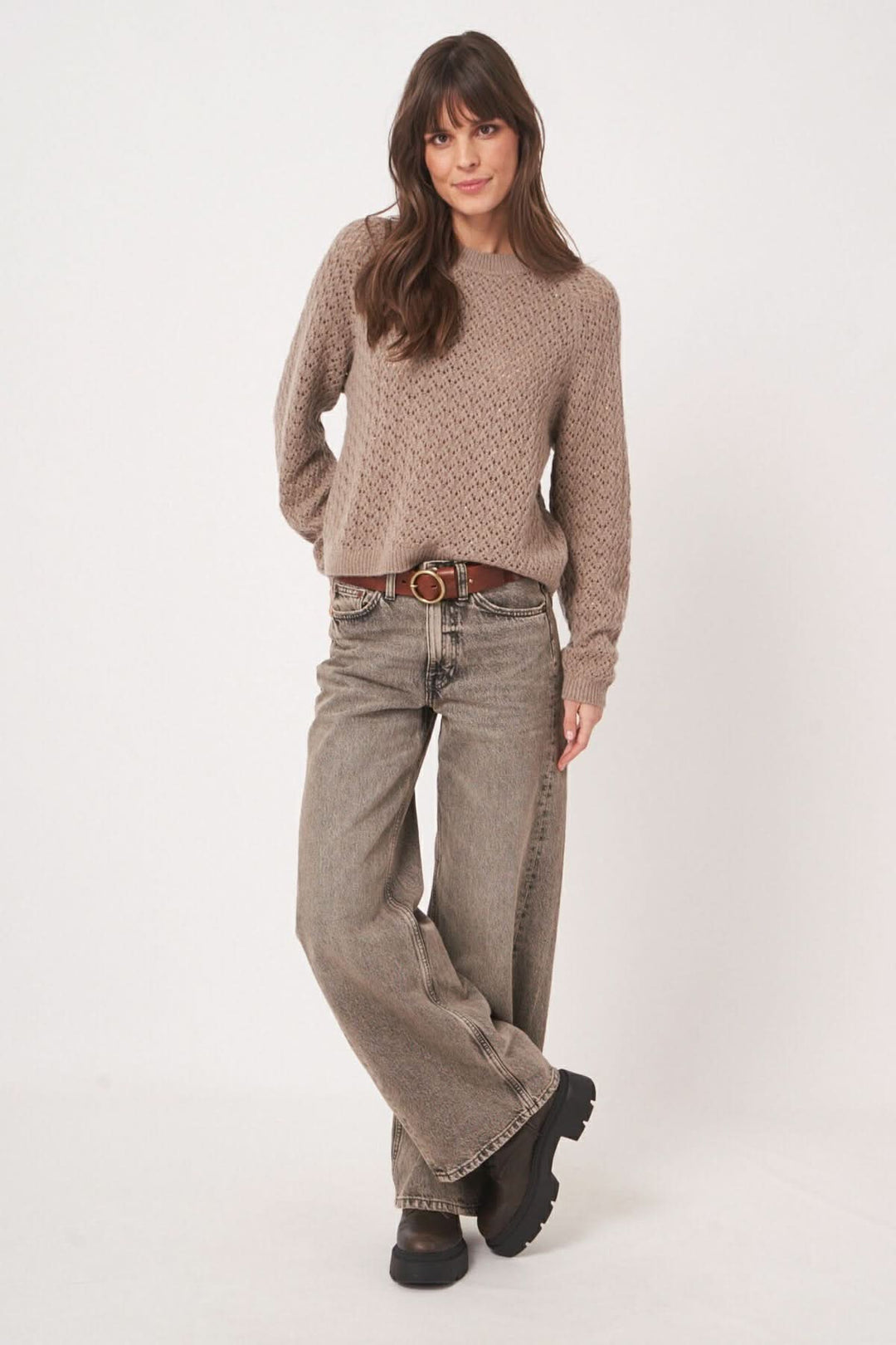 Femme portant un chandail en maille ajourée avec un jean large, style décontracté et élégant.