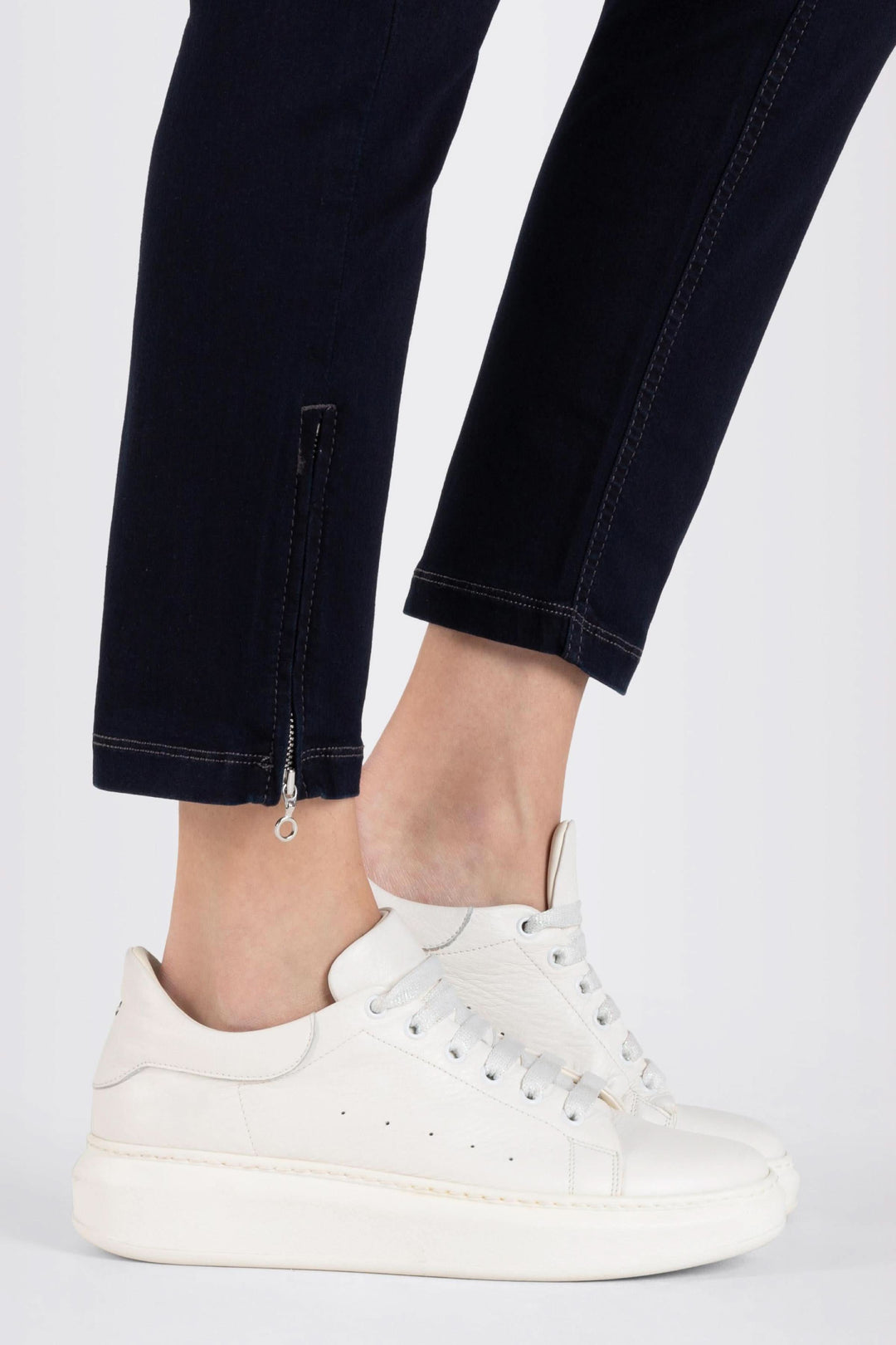 Jean ajusté 7/8 avec détail zip, porté avec sneakers blancs pour un look casual chic.