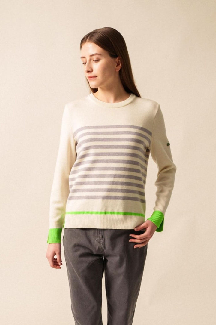 Chandail Evian à rayures grises et blanches avec finitions fluo vertes, porté avec un pantalon gris.