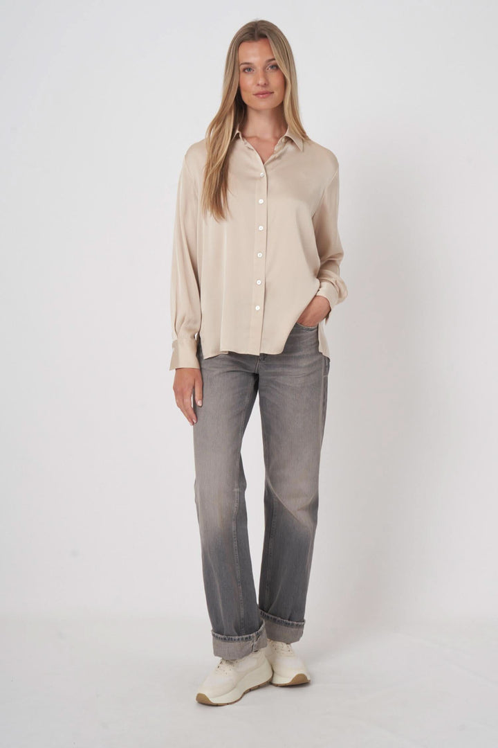 Chemise en soie fluide beige, coupe droite, portée avec un jean, style élégant et confortable.