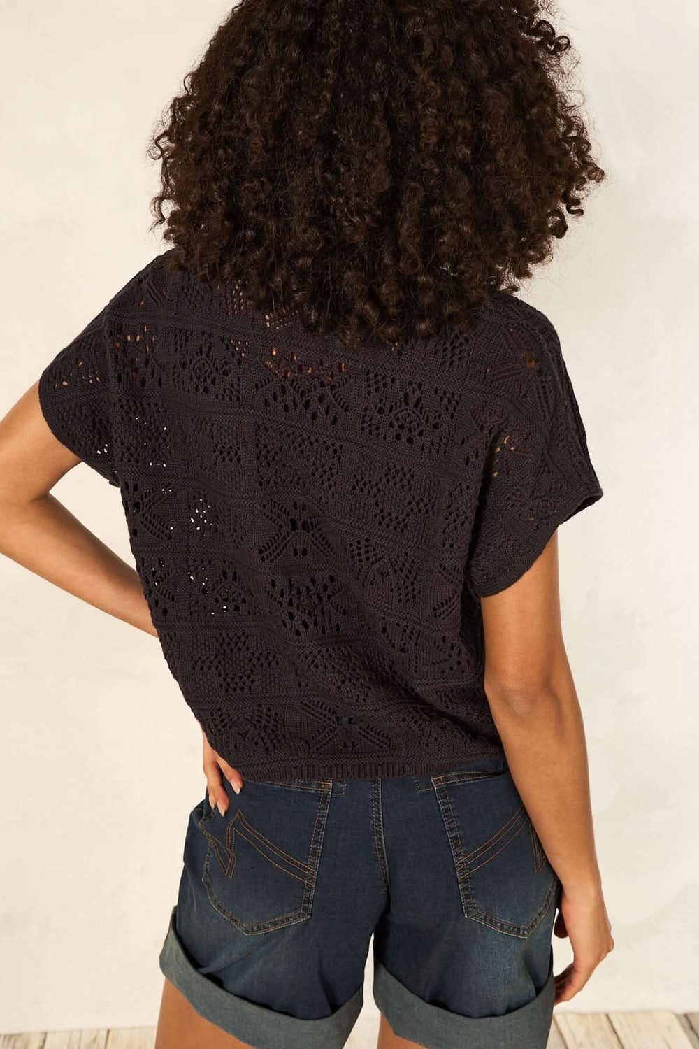 Femme portant un cardigan en maille ajourée noire, vu de dos, avec un short en denim.