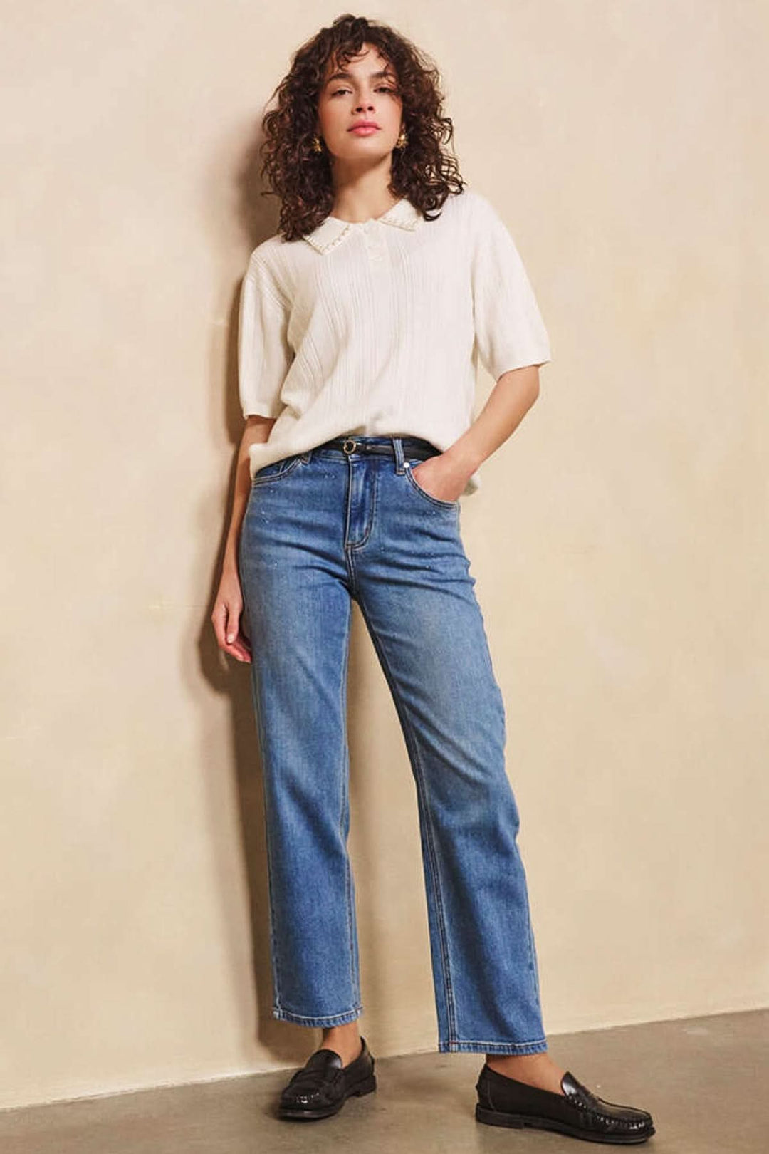 Femme portant un jean droit classique, blouse fluide beige, et chaussures noires sur fond neutre.