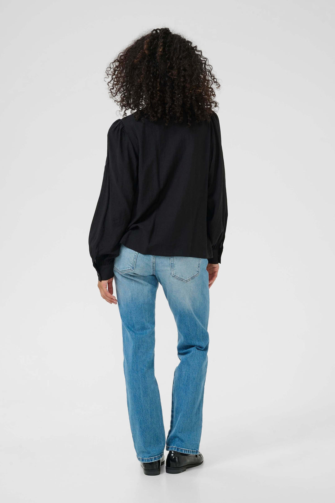 Person wearing Chemise Mirabel à col V et détails de dentelle, back view with jeans, showcasing long sleeves and buttoned cuffs.
