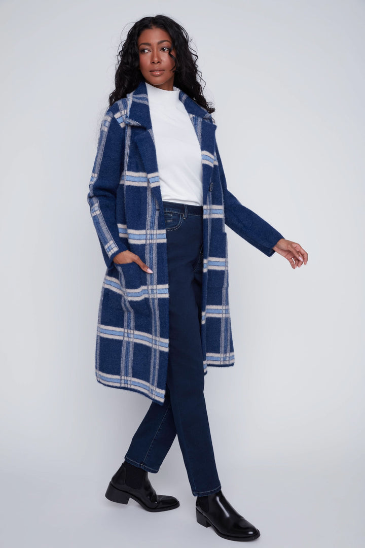 Manteau long à carreaux bleu marine, porté avec un t-shirt blanc et un pantalon ajusté pour un look chic et moderne.