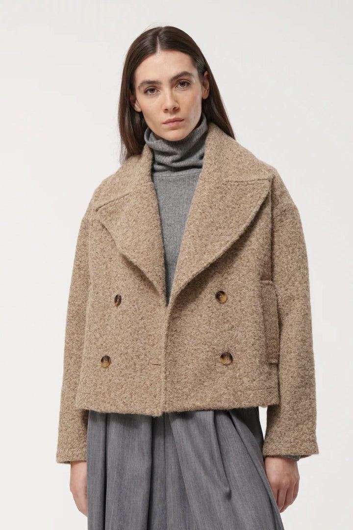 Veste courte à double boutonnage en matière texturée beige, avec col oversize, idéale pour la mi-saison, portée par un modèle féminin.