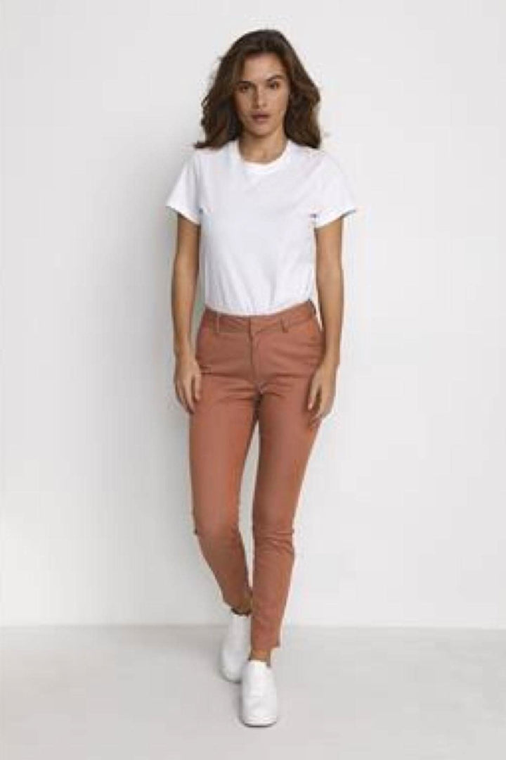 Femme portant un pantalon chino rose avec un haut blanc et des chaussures blanches, parfait pour l'été.